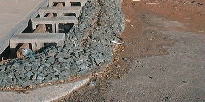 curb inlet protected with a guard made from cinder blocks and rocks